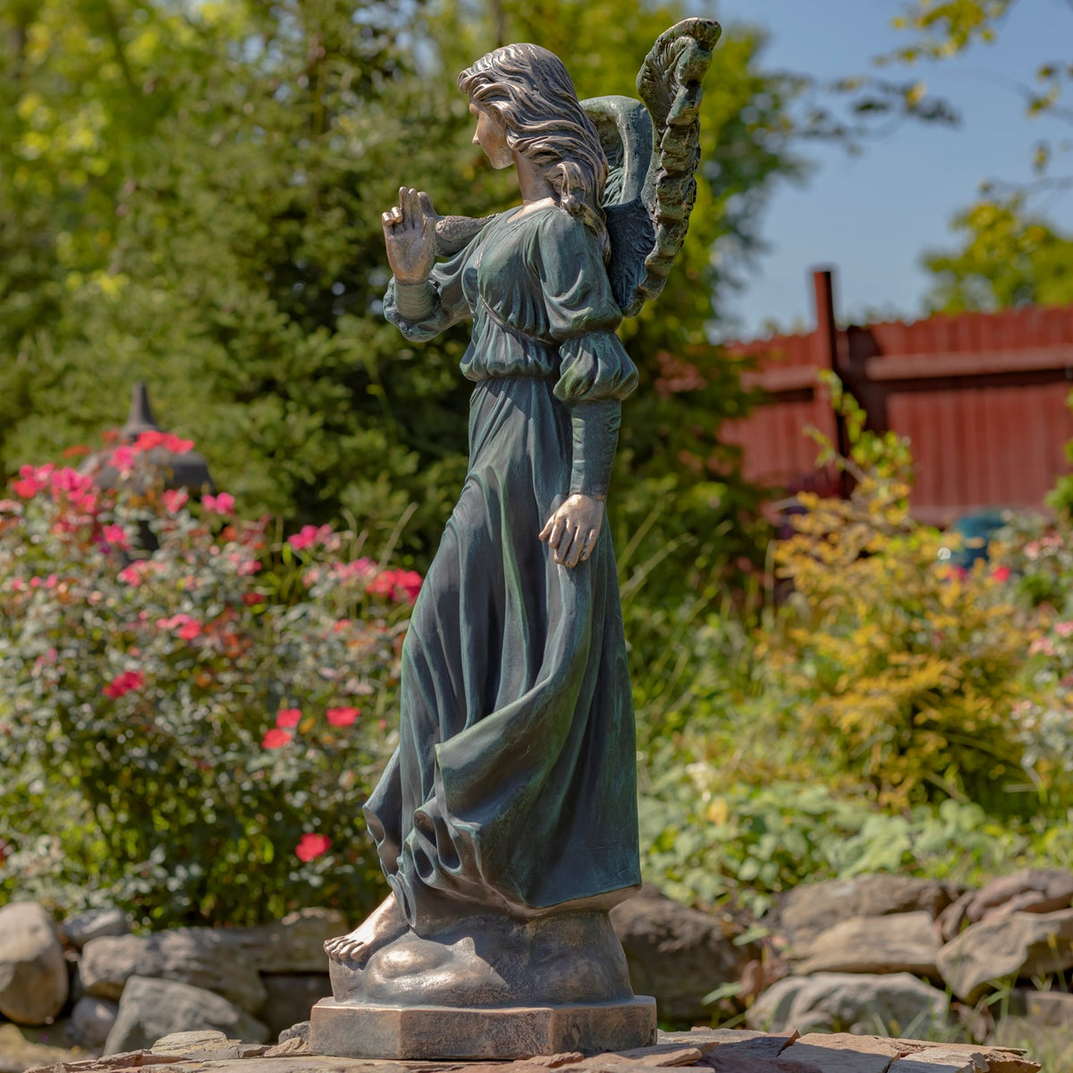 Full side view of the angel statue in a flowing robe, with one hand raised and a bird perched on her arm.