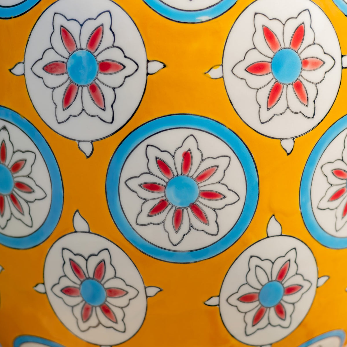 Close-up of yellow glaze decorated with white floral medallions, red petals, and blue accents.
