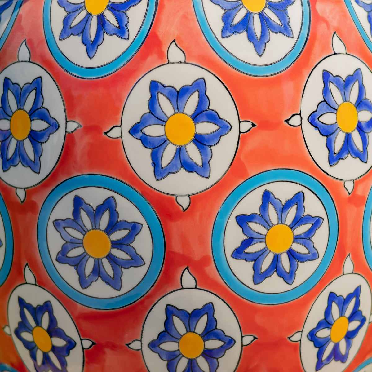 Close-up of a red ceramic surface decorated with blue and yellow flowers inside circular motifs.