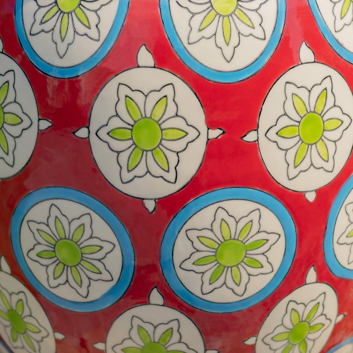 Close-up of a red ceramic surface decorated with blue-rimmed medallions and green-centered floral motifs.