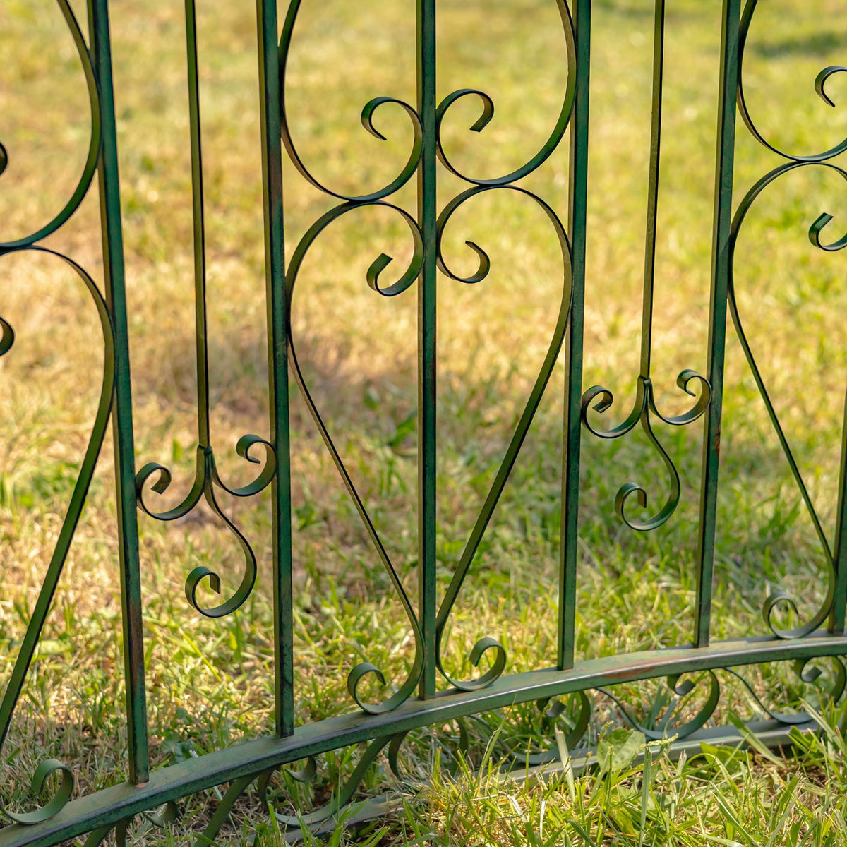 Close-up of dark green iron side-wall bars with curled scrollwork above grass.