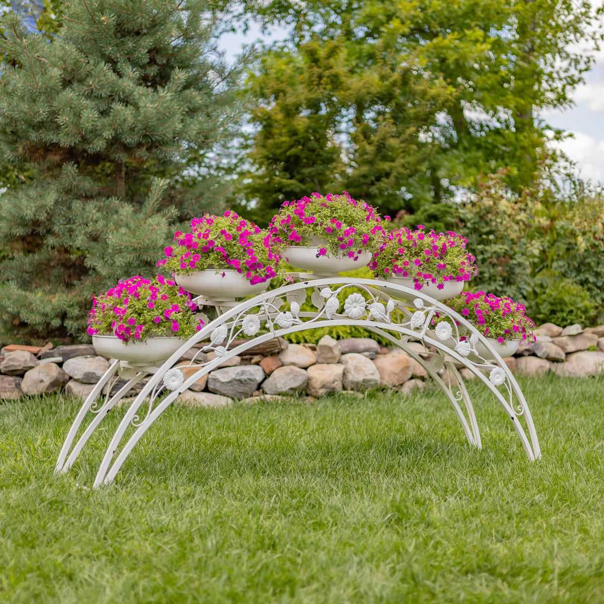 White arched metal plant stand holding five flower-filled bowls on a lawn.