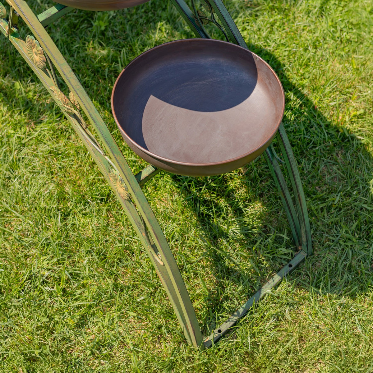 Close view of a shallow brown planter bowl resting on the curved green iron frame over grass.