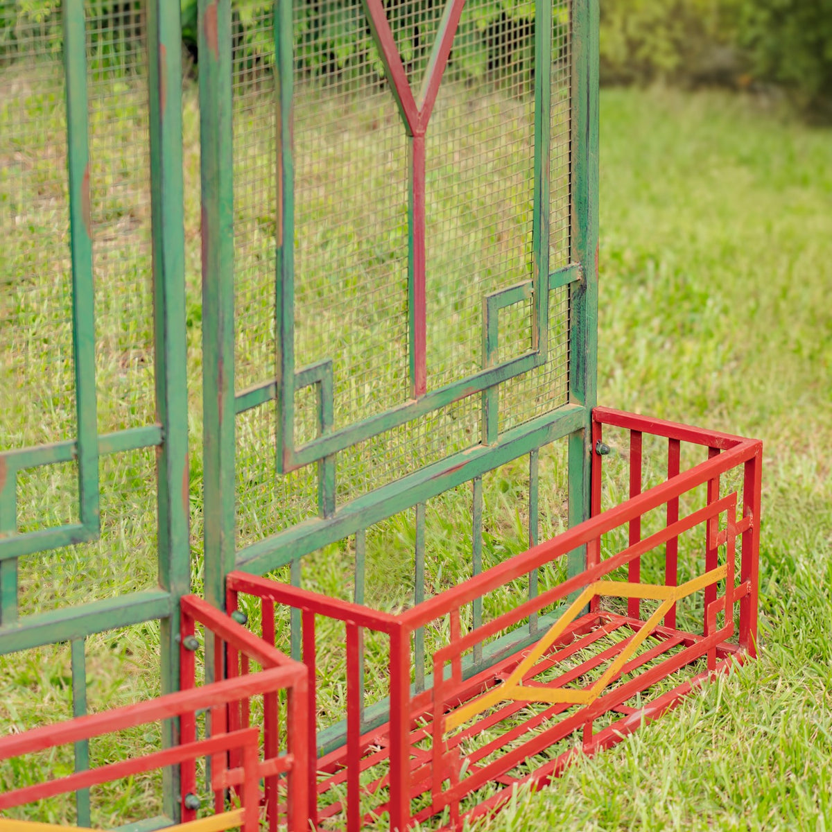Green metal gate panels stand behind red rectangular planter frames on the grass.