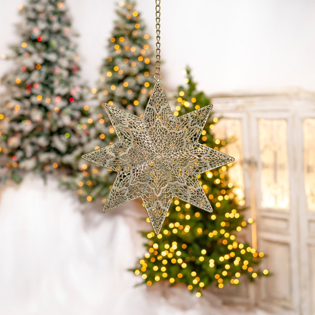 Openwork gold eight-point star ornament hanging before softly lit Christmas trees.