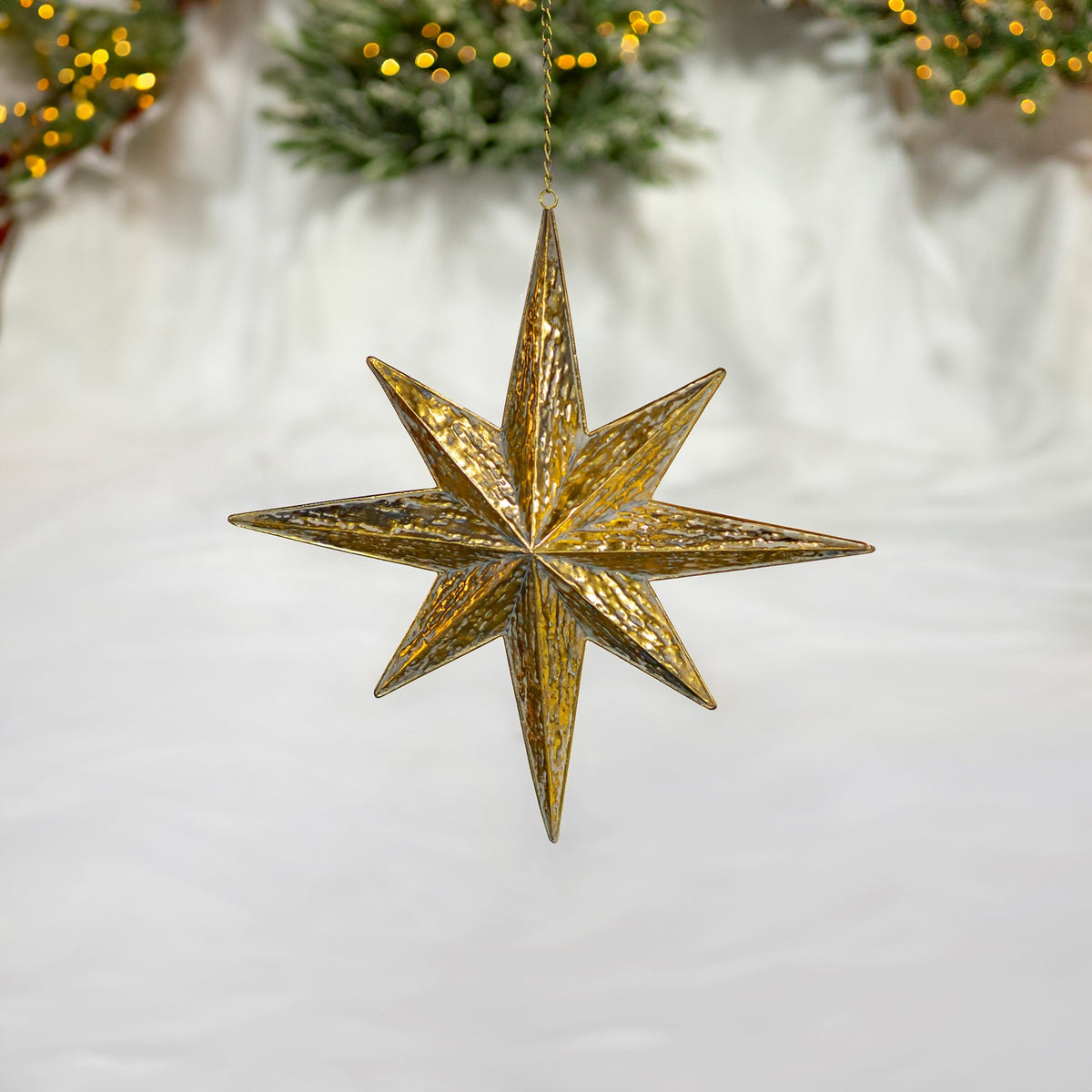 Antique-gold pointed star ornament hanging against a snowy holiday display.
