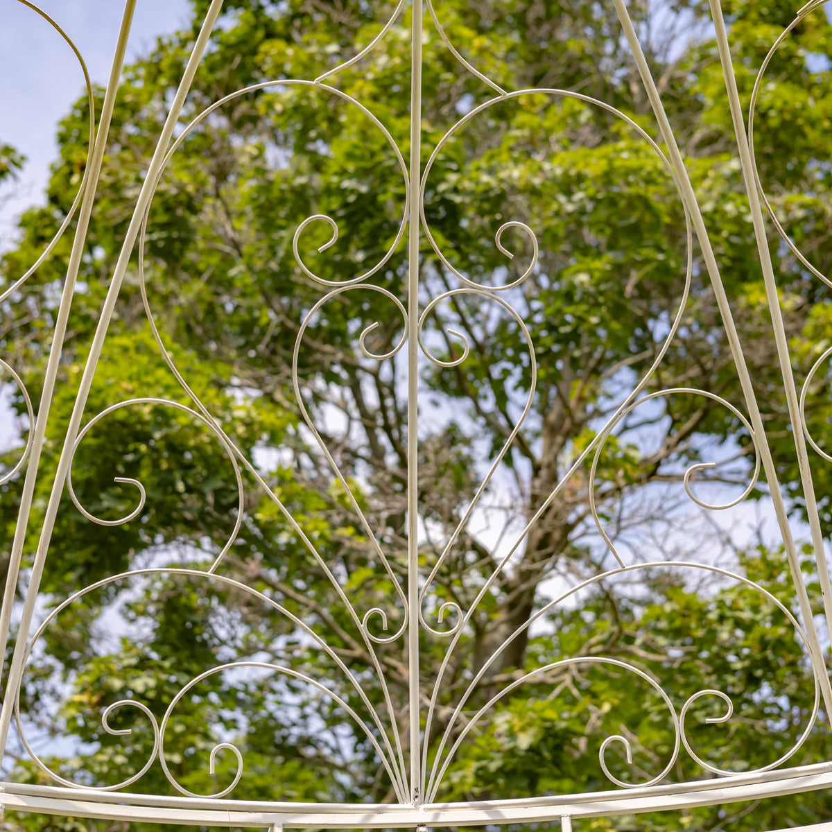 Symmetrical iron scrollwork forms a fan-like pattern between the gazebo’s curved supports.