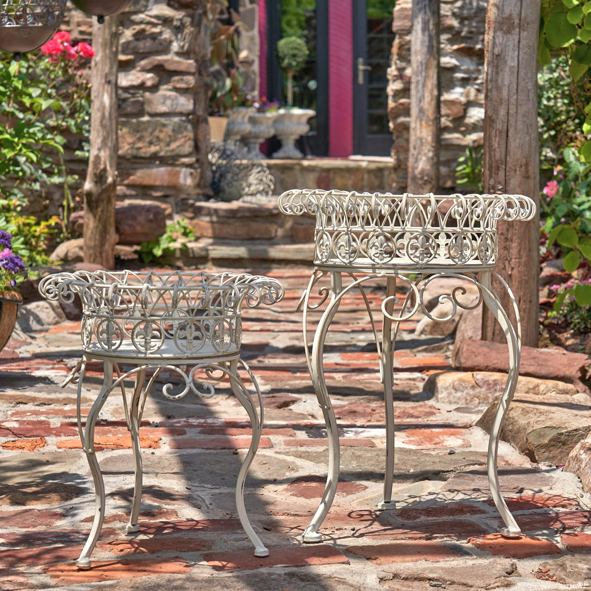 A pair of ornate metal plant stands in different heights displayed on a stone patio.