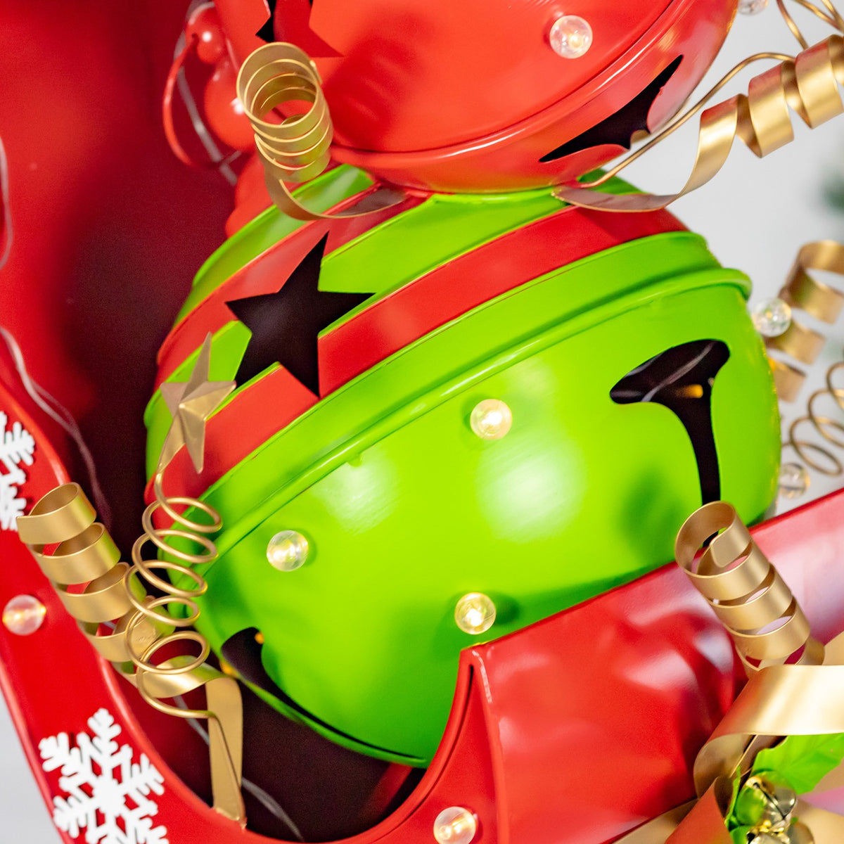 Close-up of a bright green and red jingle bell figure with gold curls and small glowing lights.