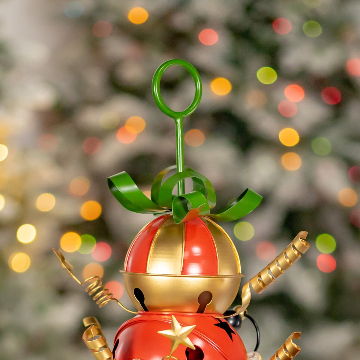 Close-up of a red-and-gold jingle bell ornament with a green bow and curled gold arms.