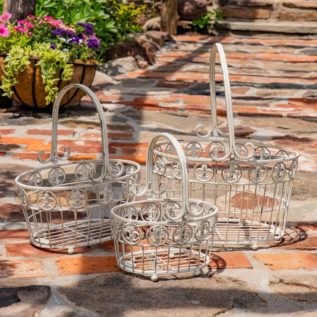 Three pale metal baskets of different sizes arranged together on a brick patio.