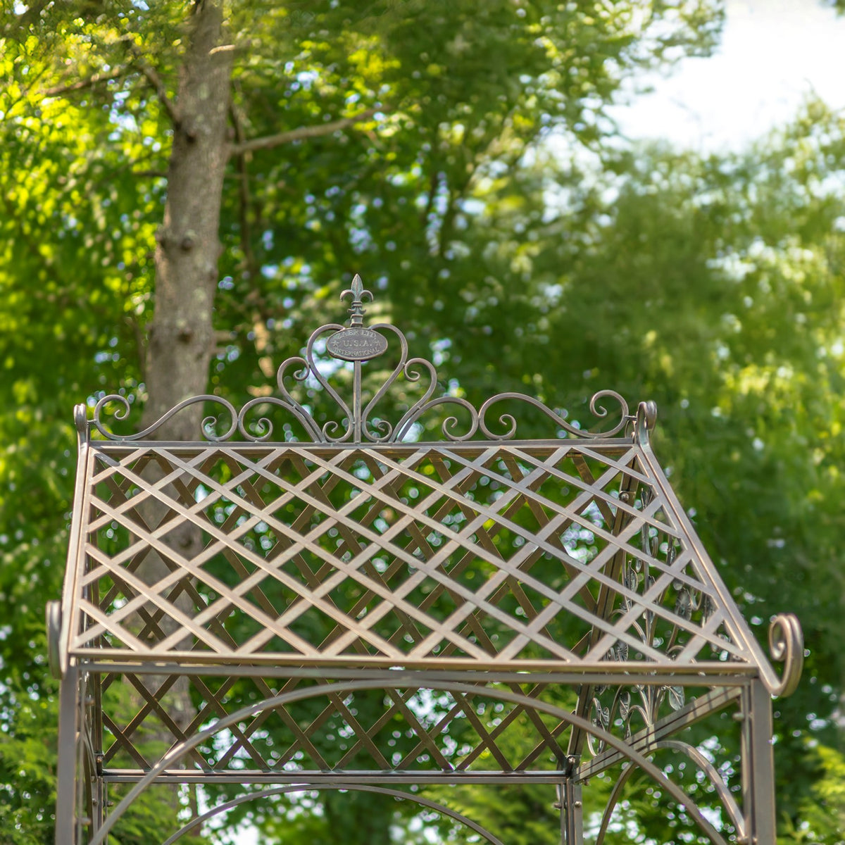 Iron arch trellis panel with diamond lattice, scrollwork crest and curved support bars in a leafy garden.
