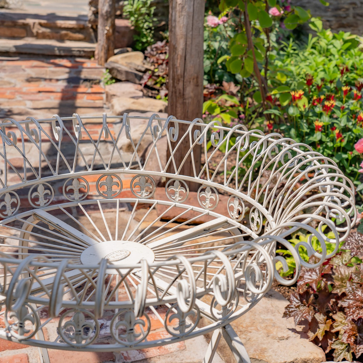 Close-up of a round stand’s pale scrollwork basket, circular motifs and radiating wire base.