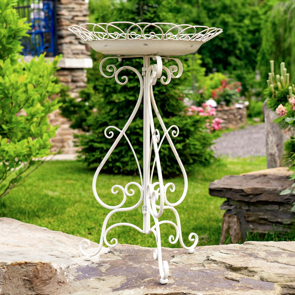 Full view of a white birdbath on an ornate folding stand in a garden.