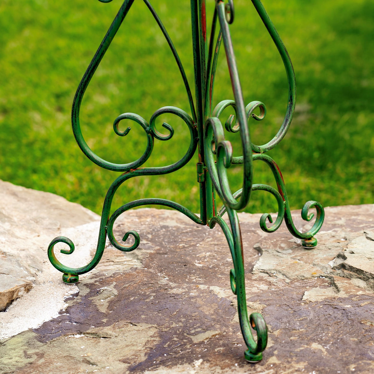 Close-up of the birdbath's curled green iron folding stand and feet on a stone patio.