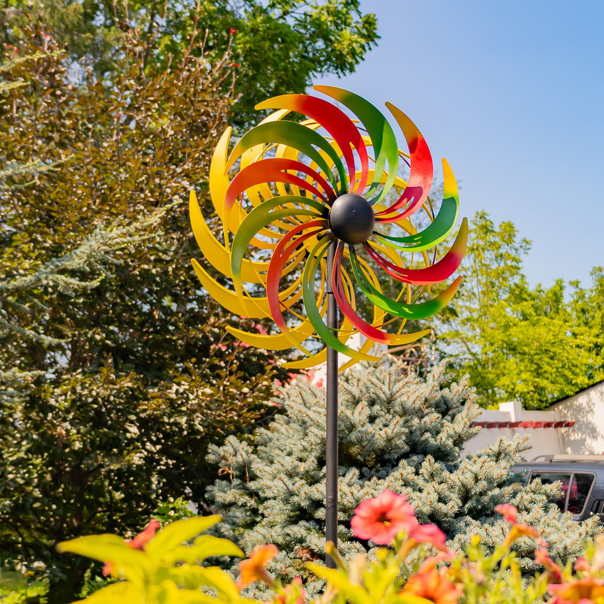 Red, green, and yellow metal windmill spinner standing among garden plants beneath a blue sky