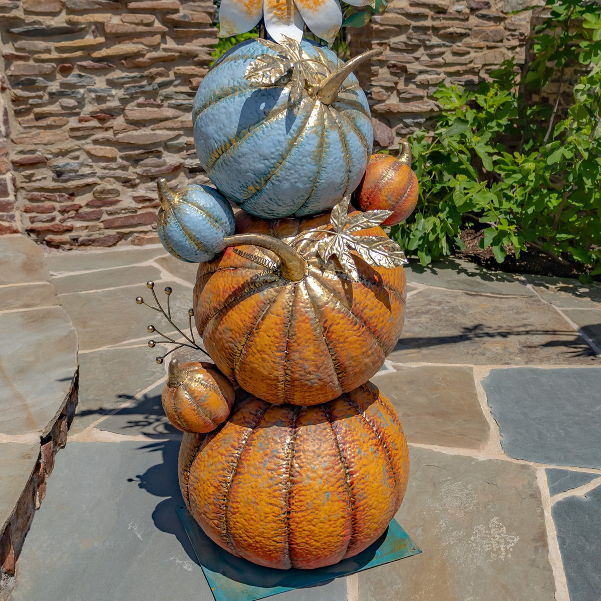 Close view of stacked orange and blue pumpkins with metallic leaf accents on a stone patio.