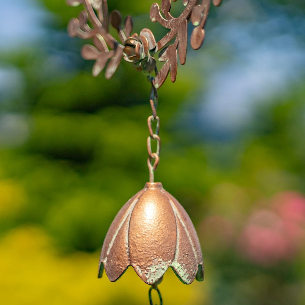 Close-up of a copper-colored metal lily bell hanging beneath part of a decorative iron wreath.