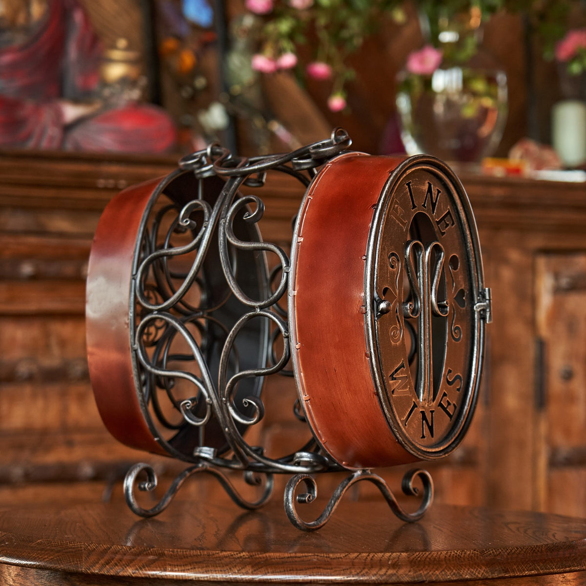 Oval barrel-shaped wine rack with ornate dark metal scrollwork and a reddish-brown side, displayed on a wooden table.