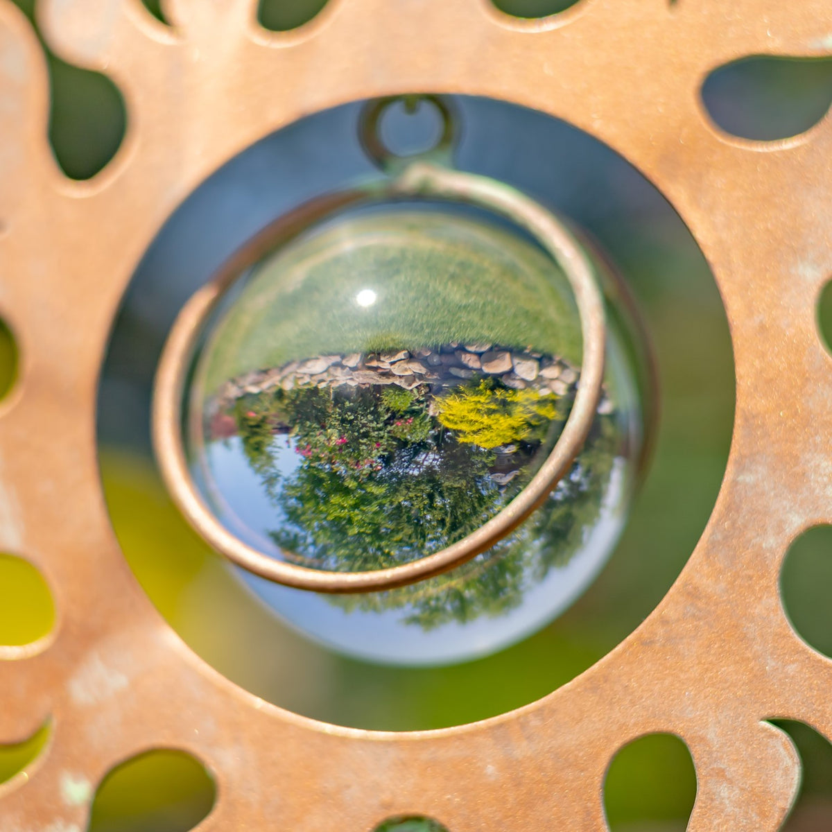 Close-up of a reflective glass orb framed by a copper-toned cutout metal ornament.