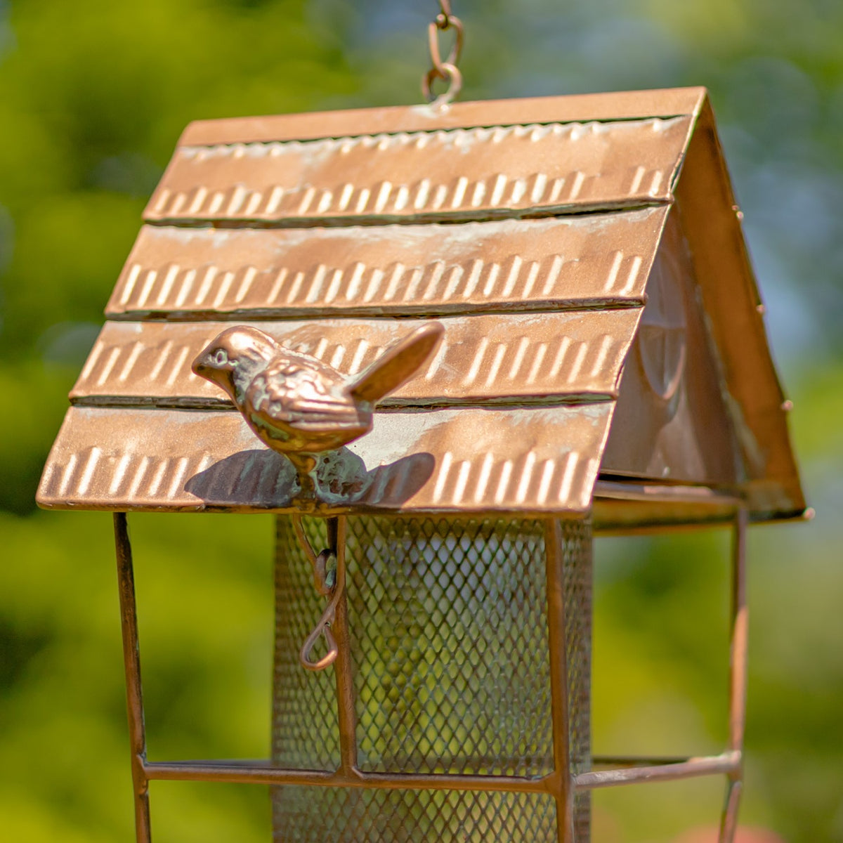 Small metal bird ornament perched on the feeder's ridged roof