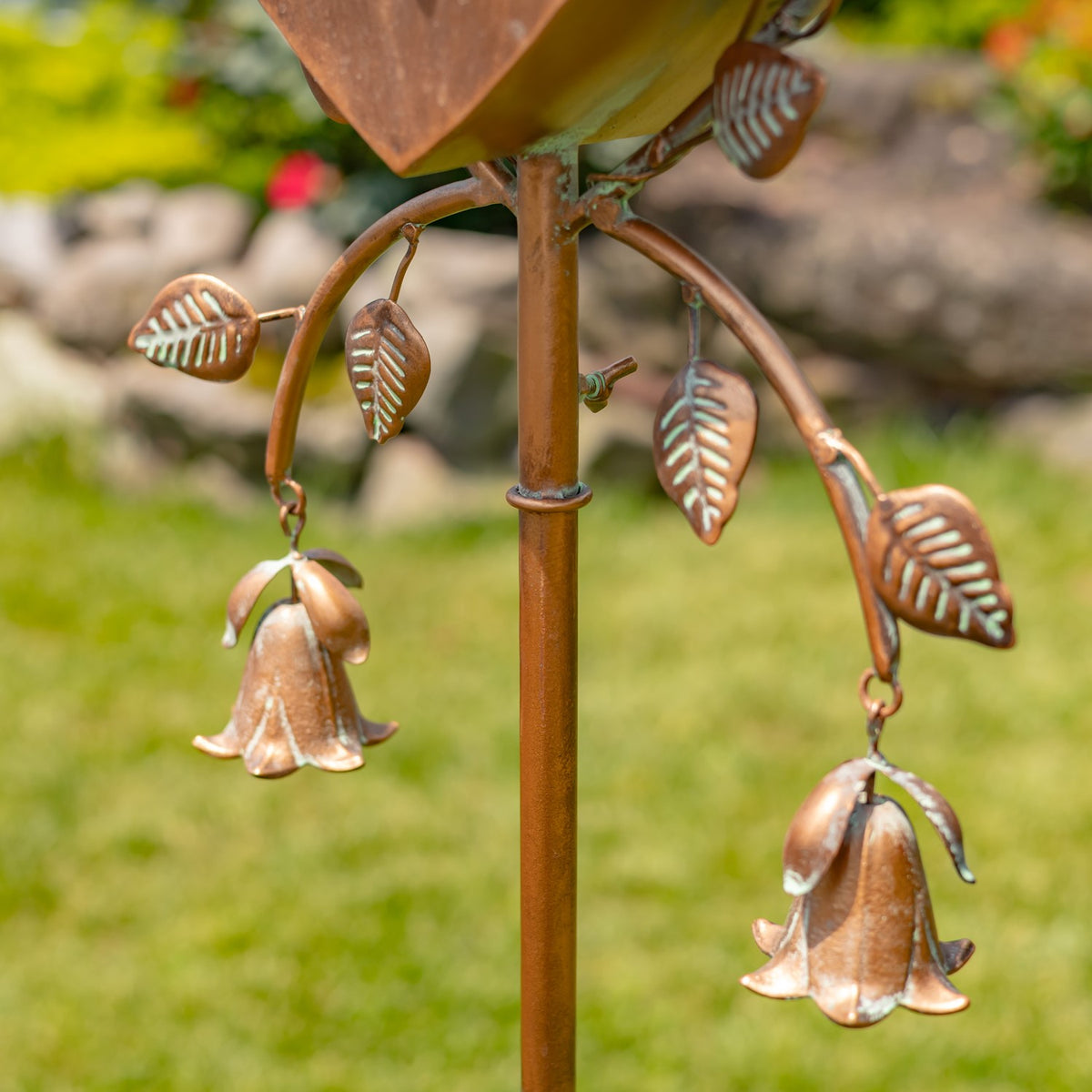 Close-up of two copper-toned bell ornaments hanging from curved branches with decorative metal leaves.