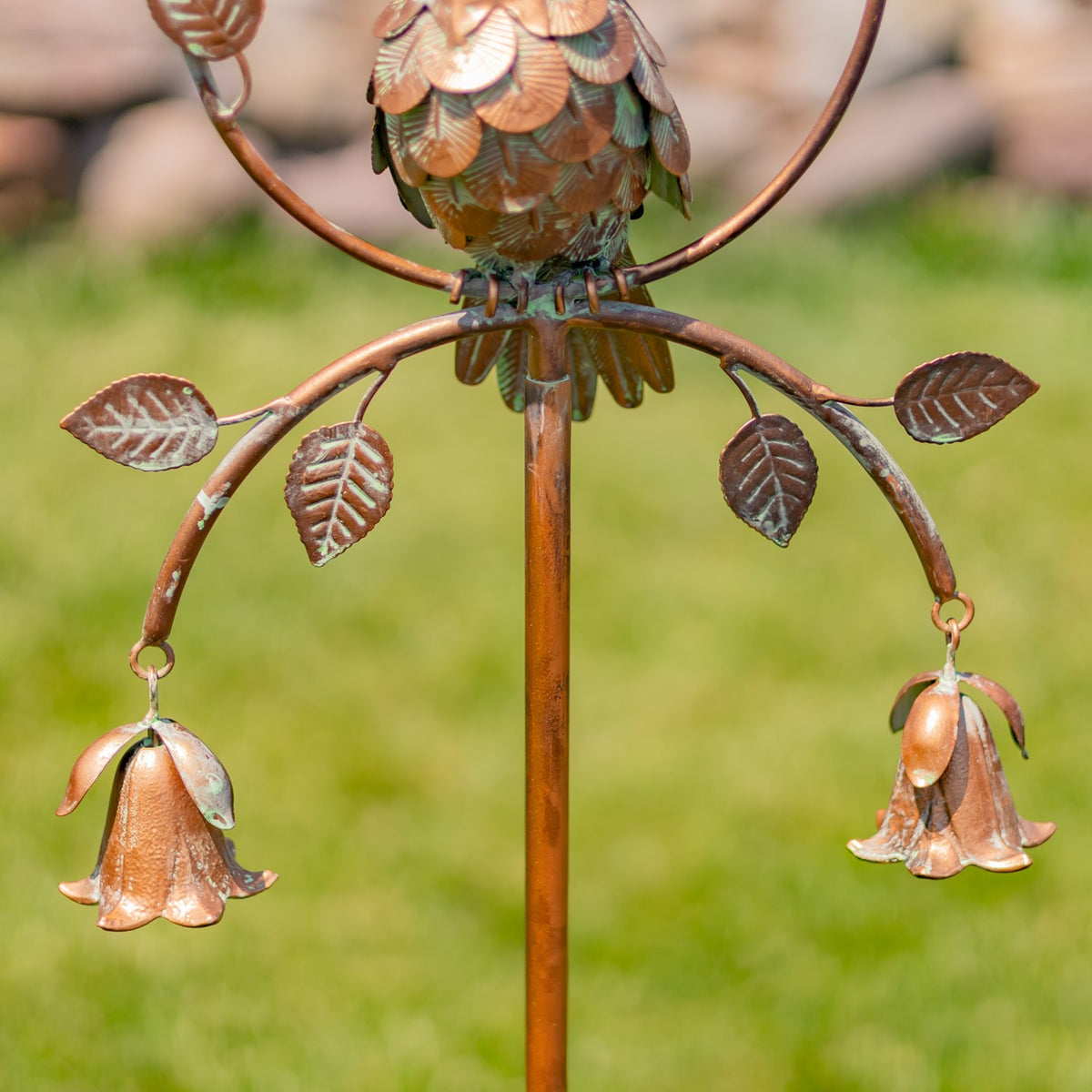 Close view of the metal cockatoo’s feet, leafy branches, central stake, and two dangling bell ornaments.