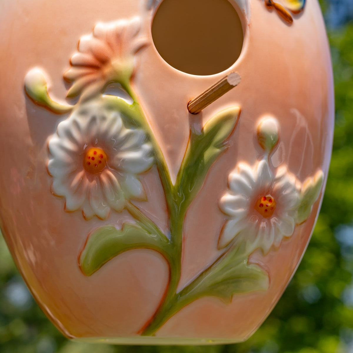 Close-up of a peach birdhouse with raised white flowers, green leaves, and a round entrance hole.