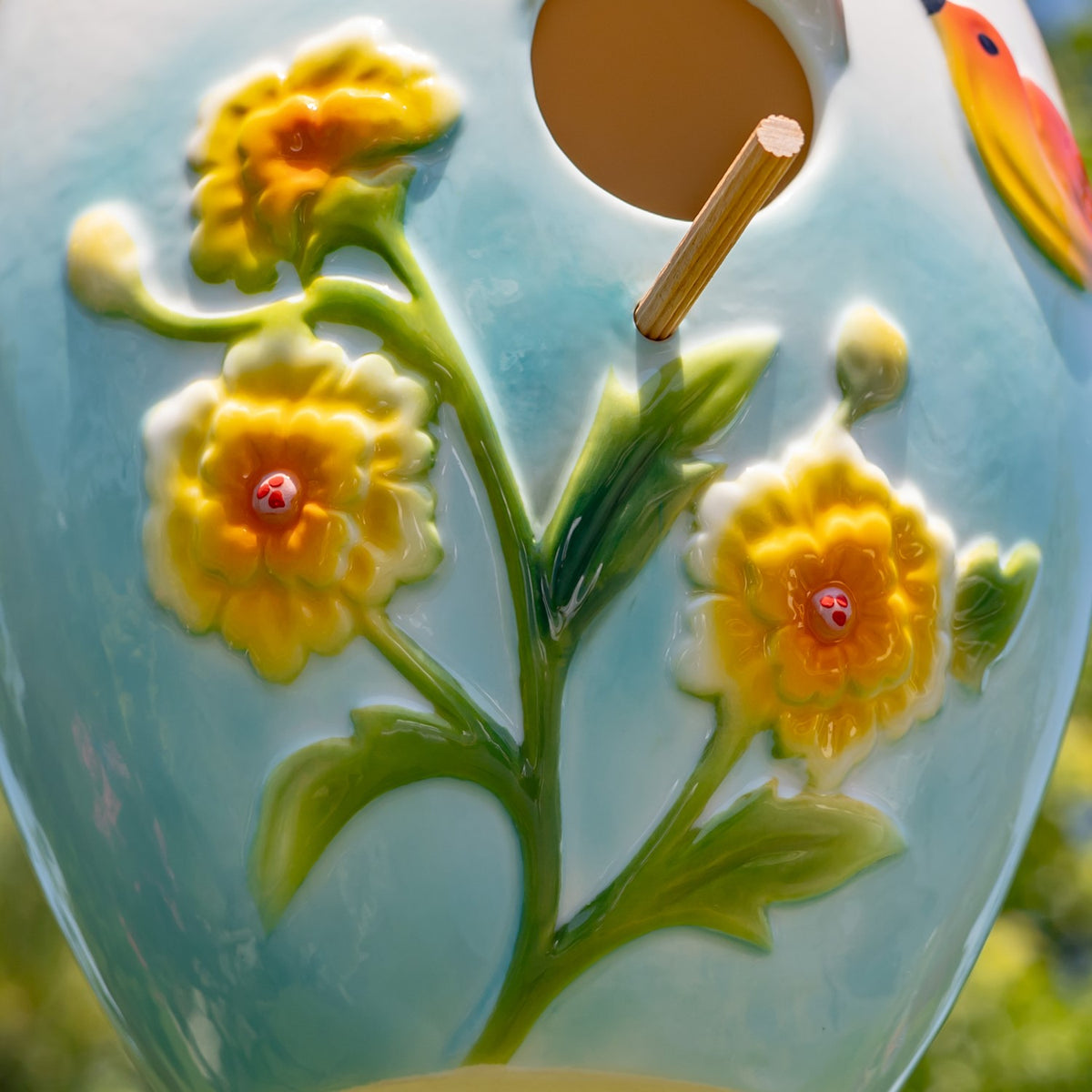 Close-up of raised yellow flowers and green leaves on a pale blue birdhouse, beside its round entrance.
