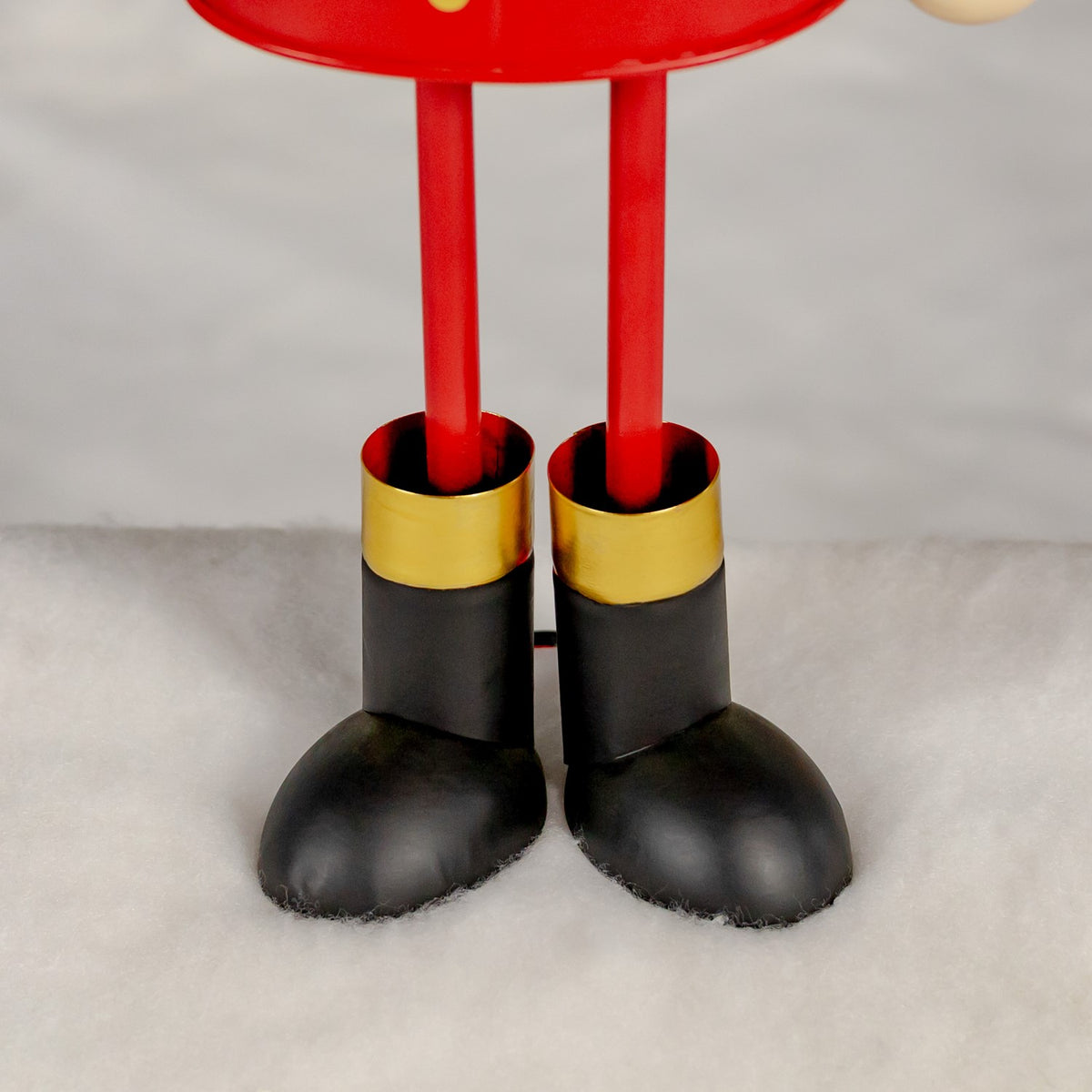 Close-up of a red figurine's slim legs, gold-trimmed black boots, and rounded toes on a white surface.