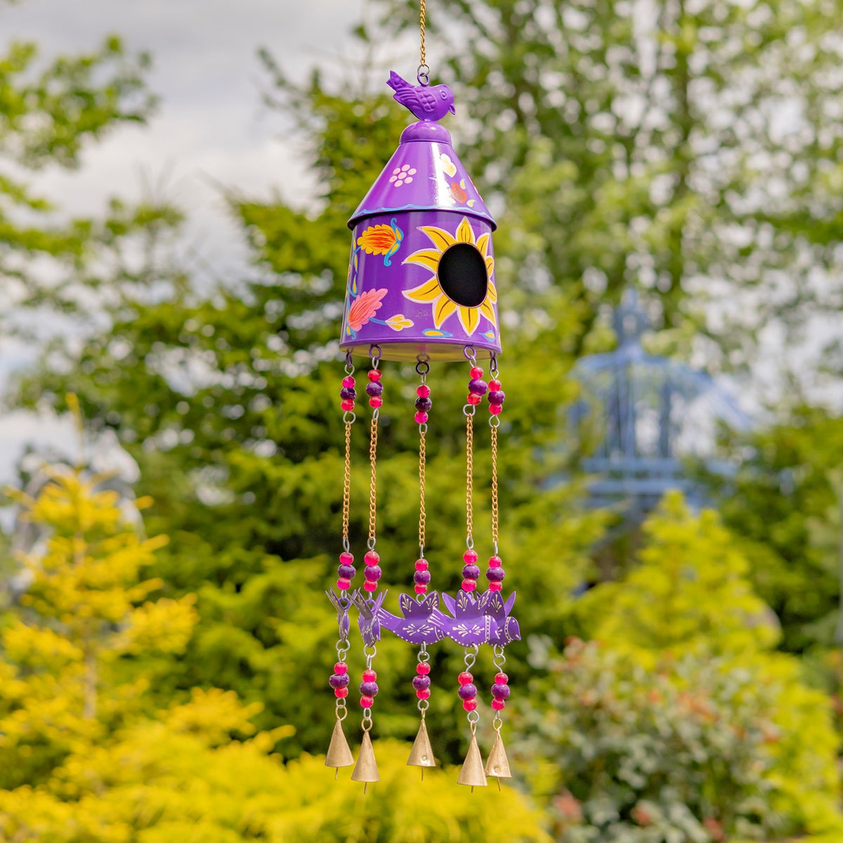 Purple birdhouse wind chime with bright floral accents and pink-beaded strands outdoors.