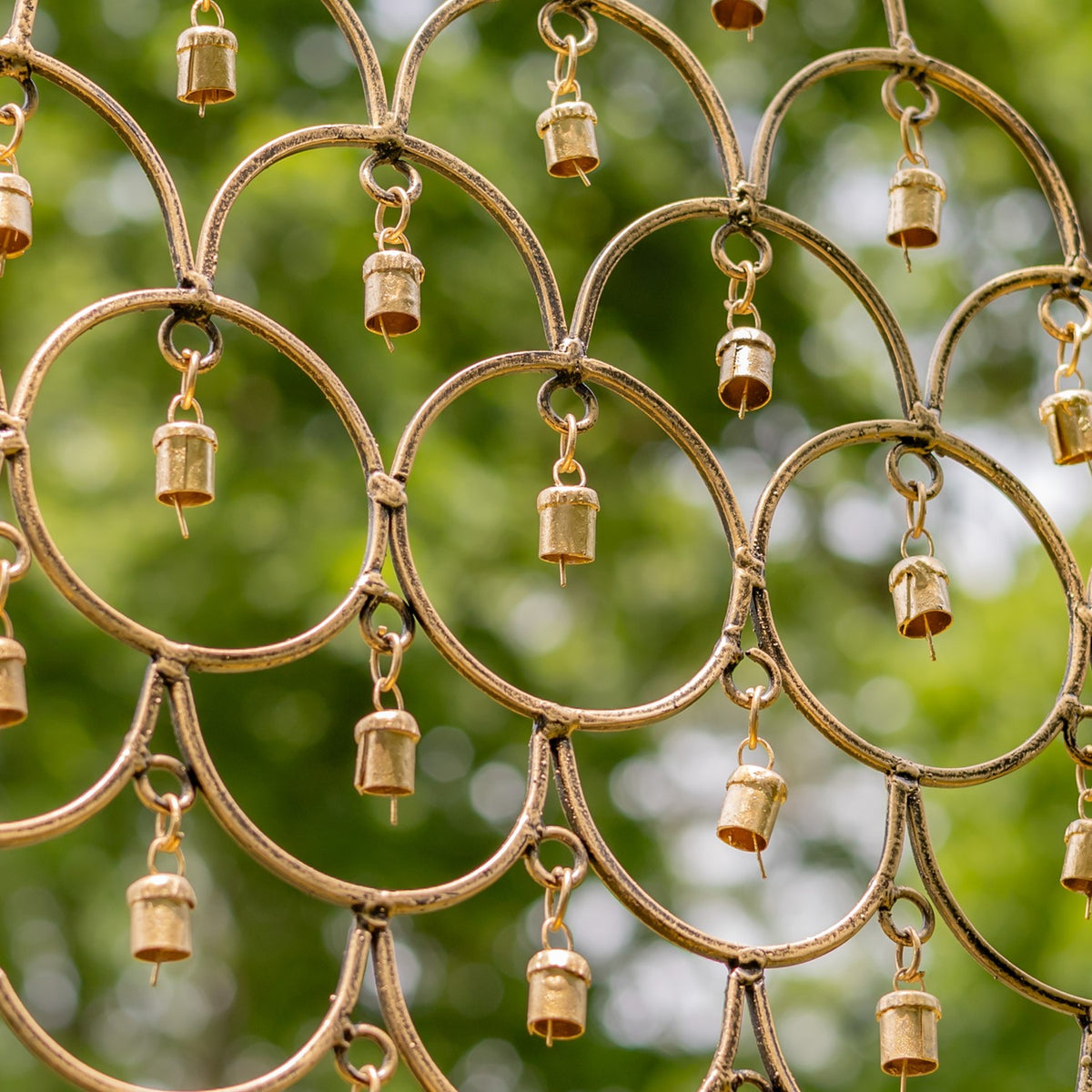 Close-up of overlapping gold-toned metal loops with small hanging bells against green foliage.