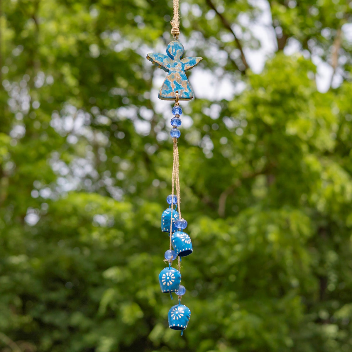 Blue angel wind chime with dangling bells hanging against a leafy green background.