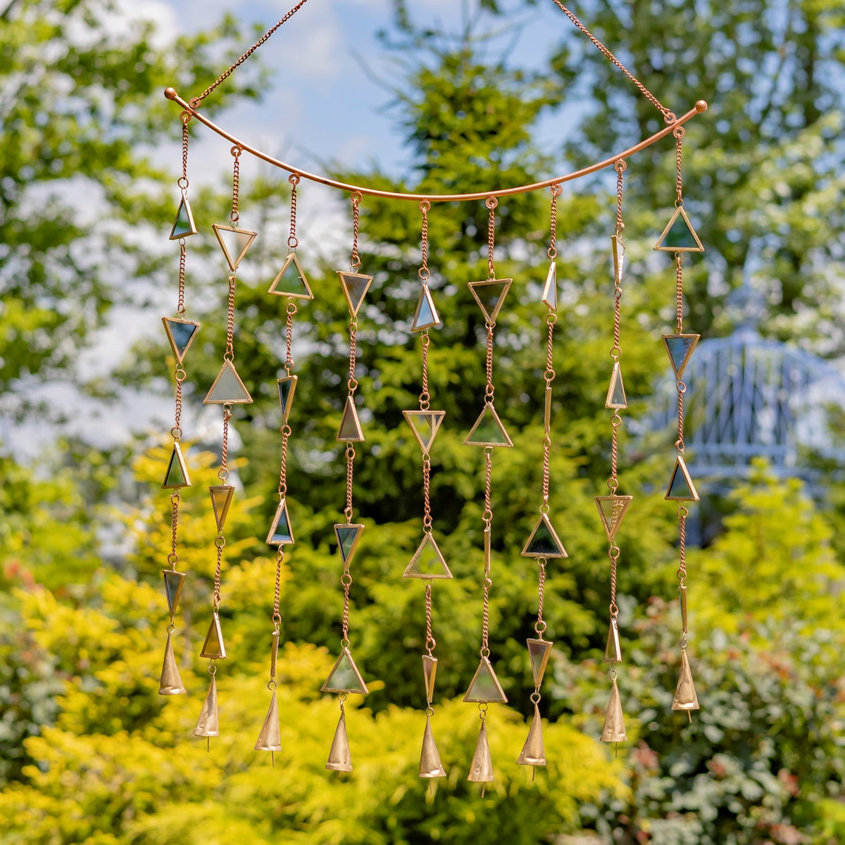 Gold-toned hanging chime with cascading chains, triangular metal pieces, and small bells outdoors.