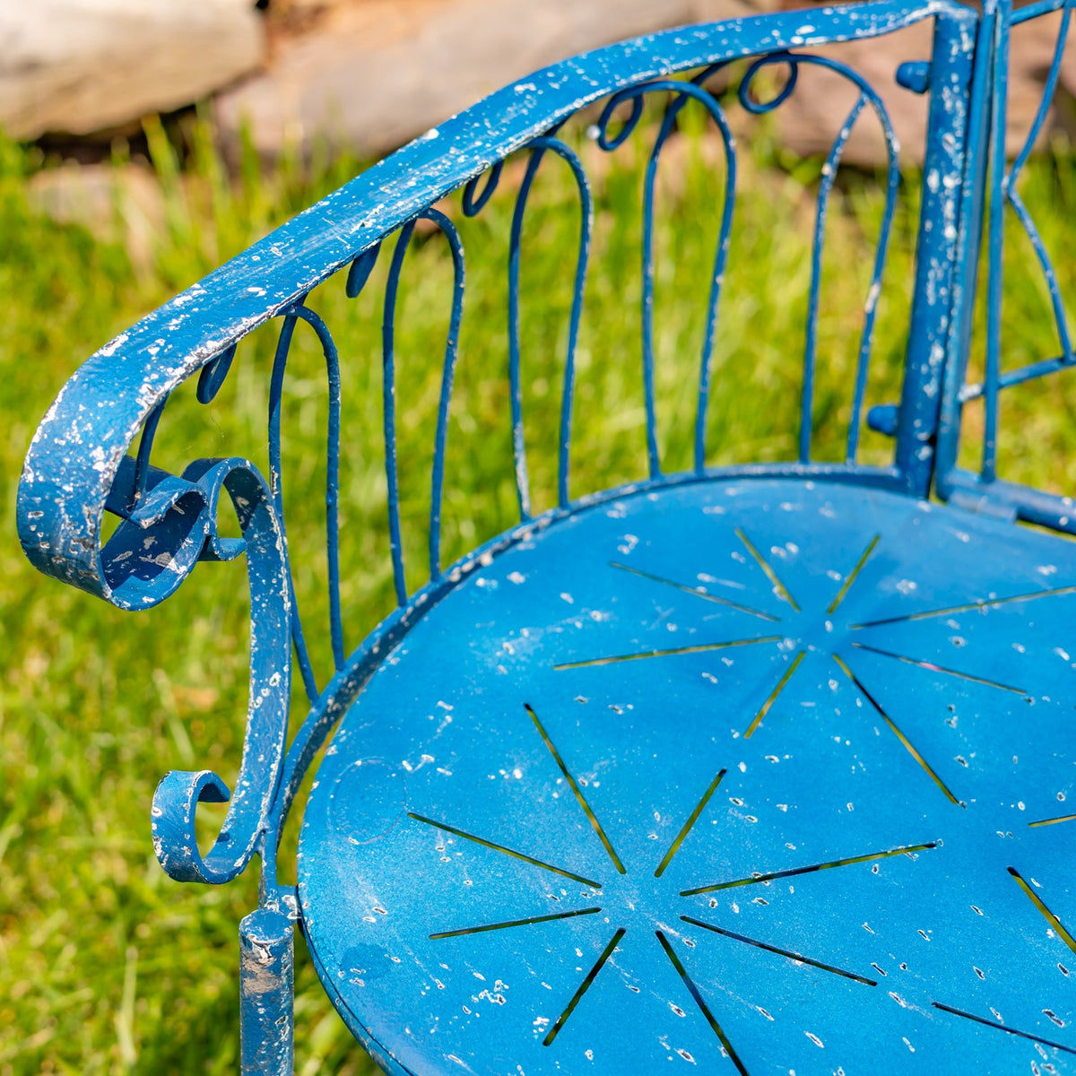 Detailed view of the distressed blue finish, curled arm, and patterned iron seat