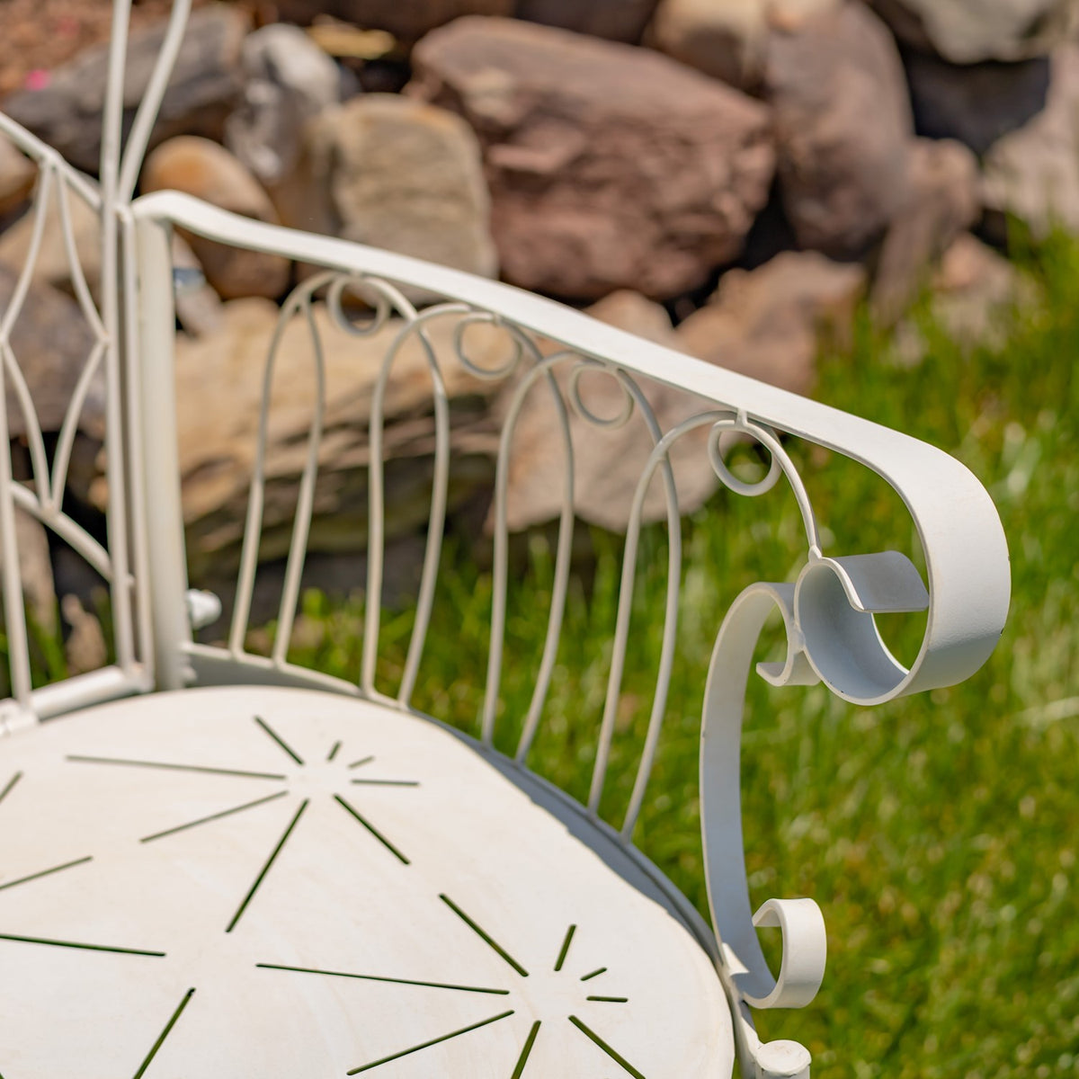 Close-up of the chair’s curled armrest, slender metal back spindles, and cutout seat pattern.