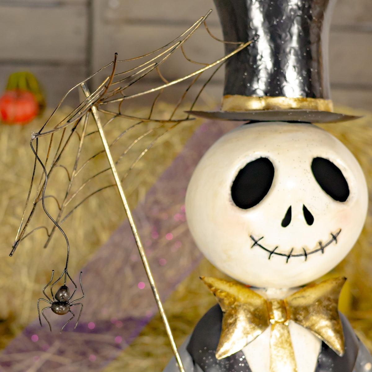 Close-up of a smiling skeleton’s top hat and gold bow tie beside a webbed umbrella with a dangling spider.