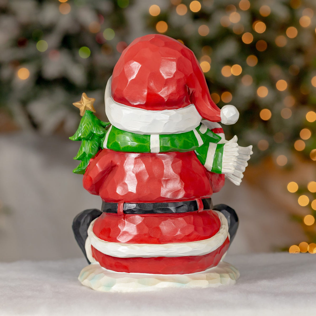 Back of the festive figurine shows a snowman in a red Santa suit and green scarf holding a small tree.