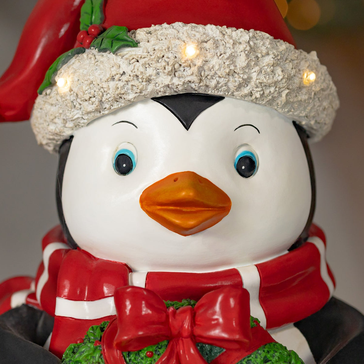 Close-up of a penguin’s face, Santa hat and red scarf, with small lights glowing along the hat brim.