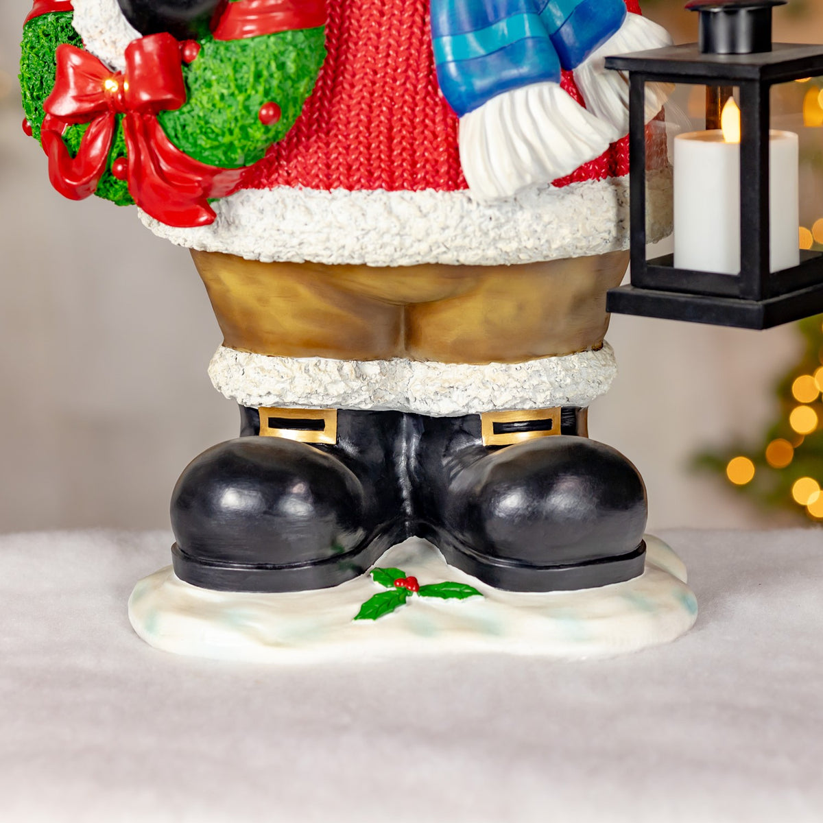 Close-up of the moose’s black boots, snowy base, and lit lantern beside its red sweater.