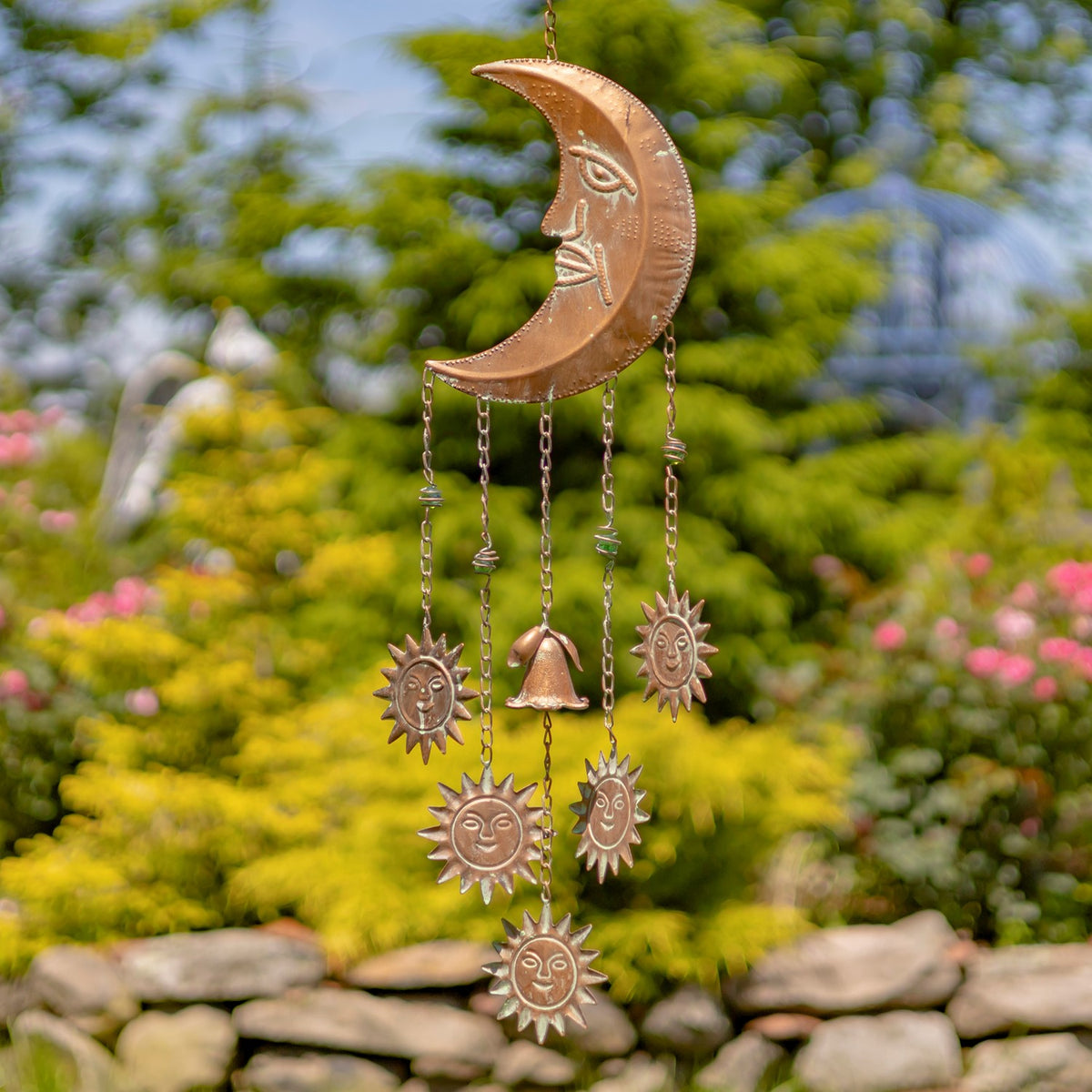 A crescent moon wind chime hangs outdoors, with sun-shaped pendants and a small bell dangling below.