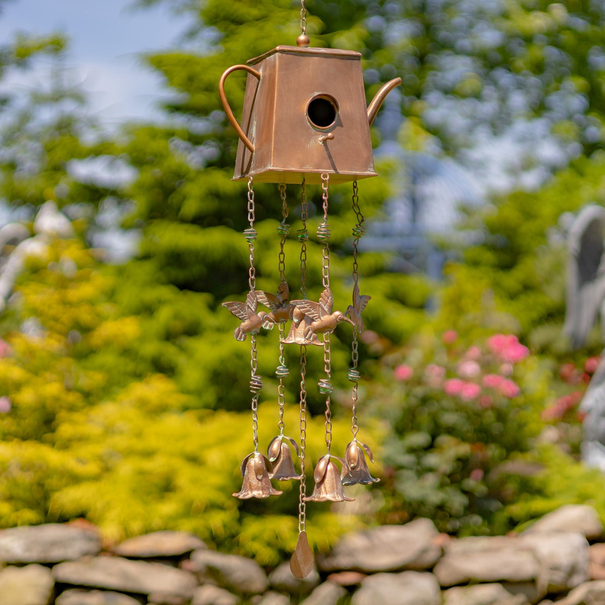 Angular copper-colored teapot birdhouse wind chime hanging outdoors, with bird ornaments, bells, and a drop-shaped pendant.