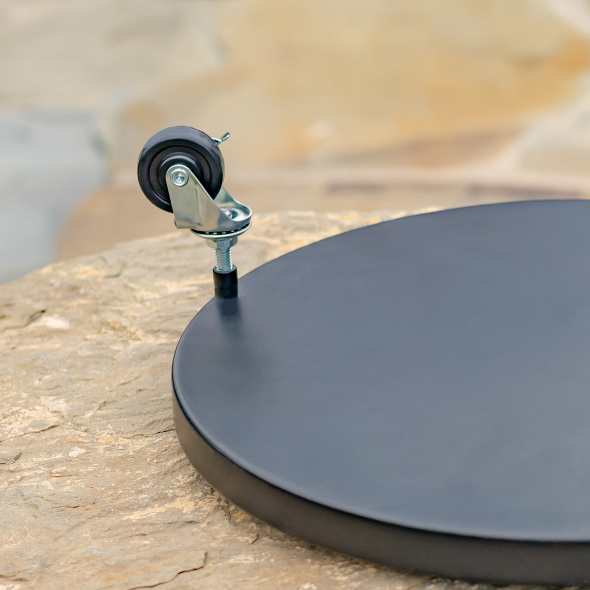 Close-up of a caster attached to the edge of a smooth, dark round plant trolley.