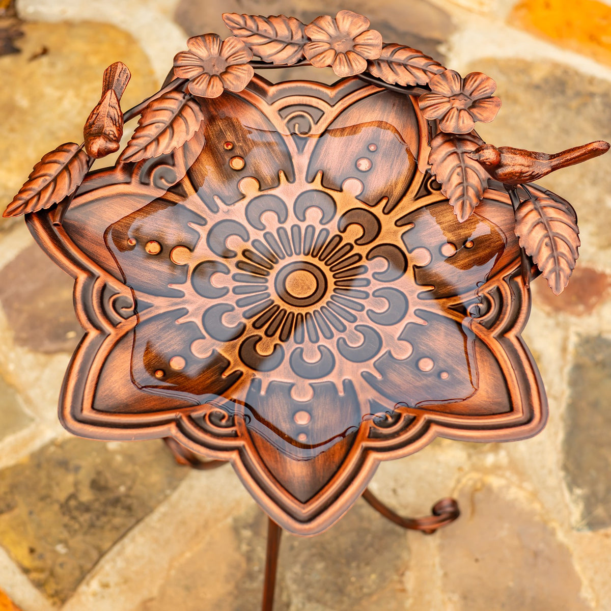 Antique-bronze birdbath bowl with a mandala pattern, flower-and-leaf trim, and two bird figures on the rim.