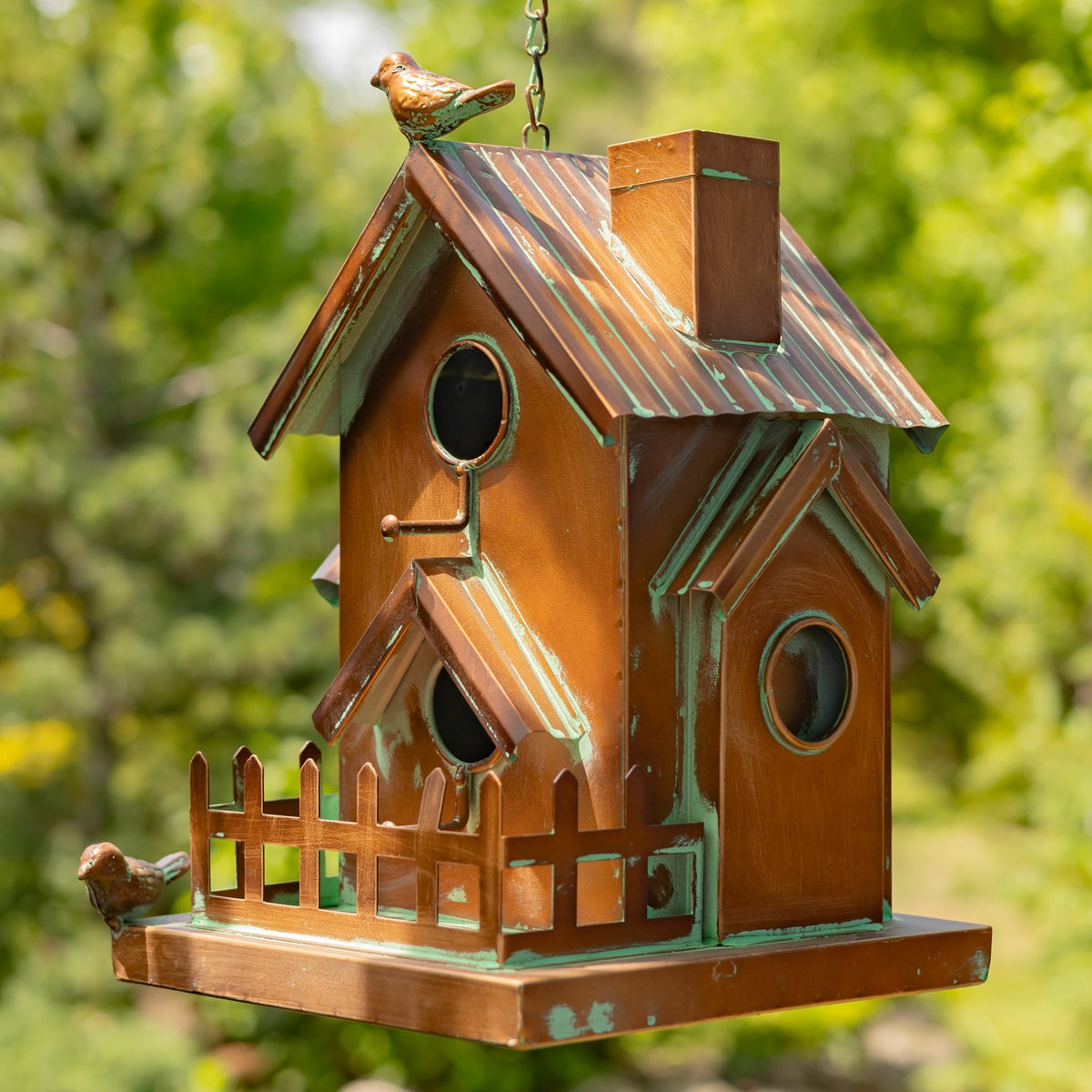 Copper-toned hanging birdhouse with several roof sections, round openings, a fence, and decorative birds.