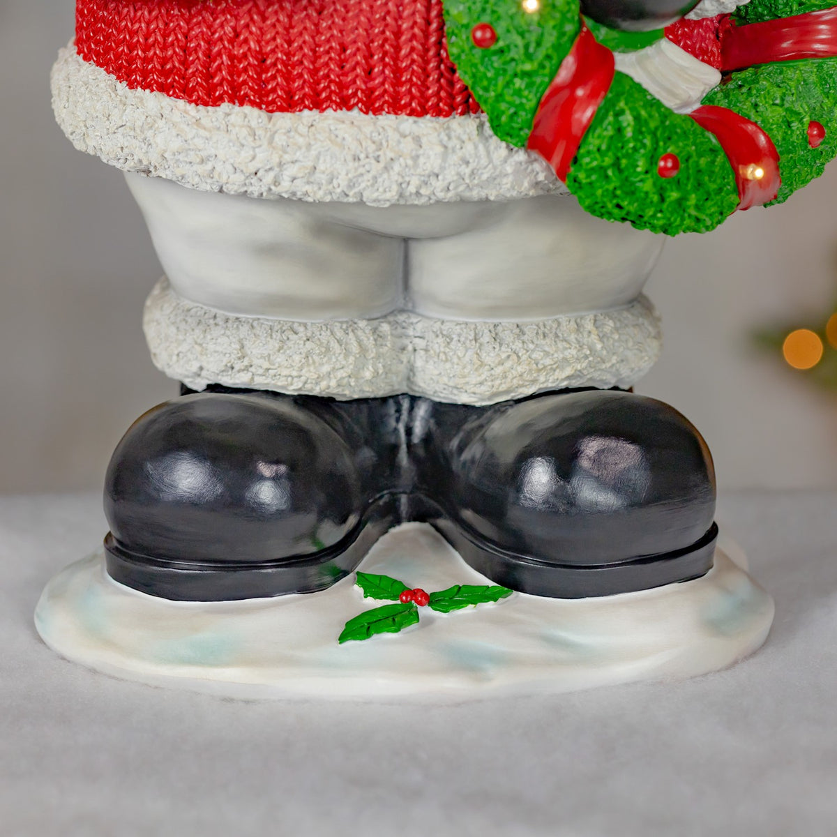 Close-up of black boots on a snowy base, with holly leaves between them.