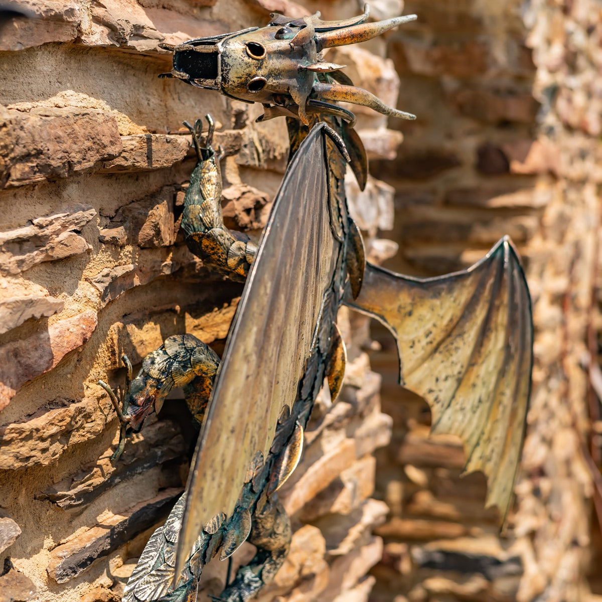 Metal dragon decoration with outstretched wings mounted on a rough stone wall, seen from the side.