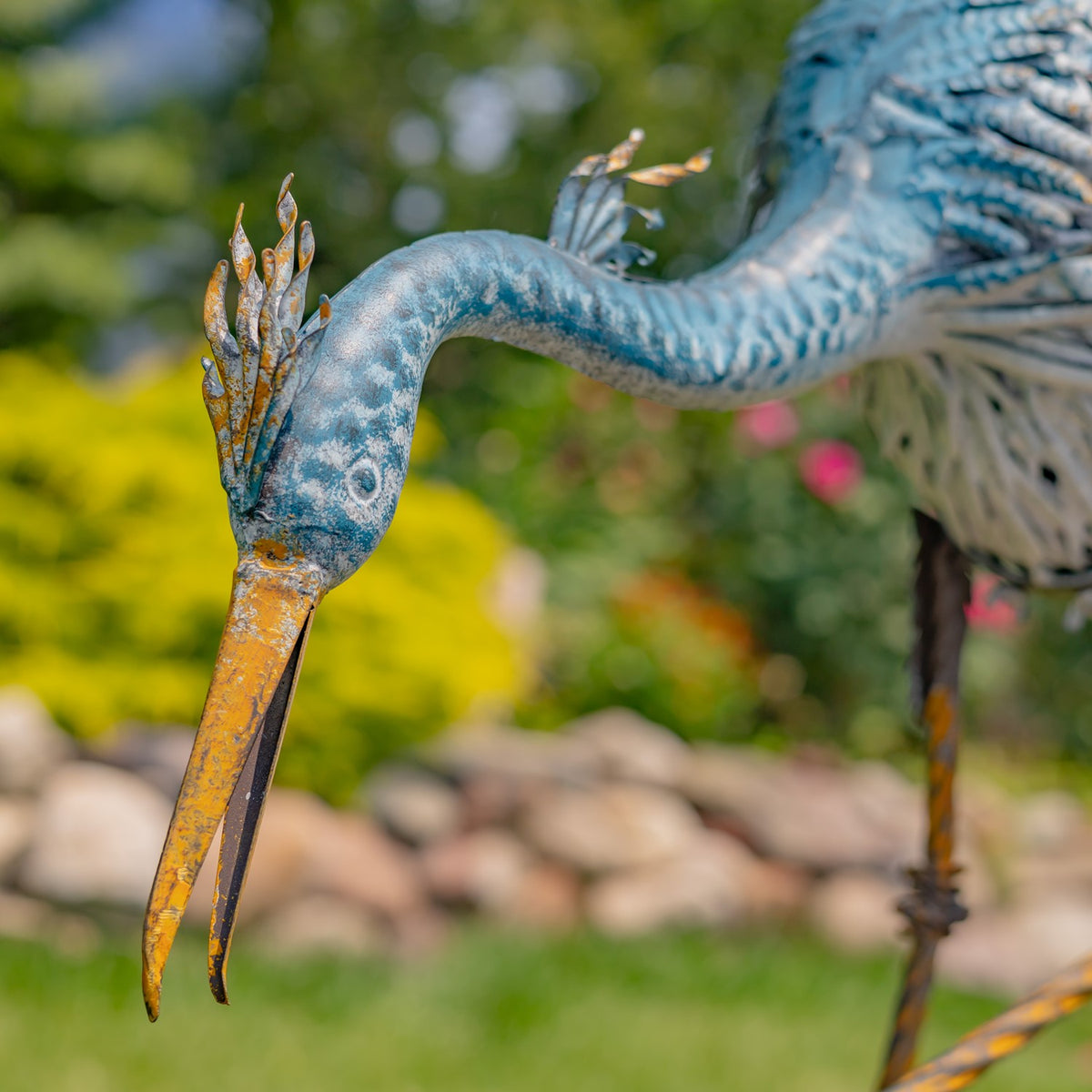Close-up of a heron figurine's head and long orange beak against a garden