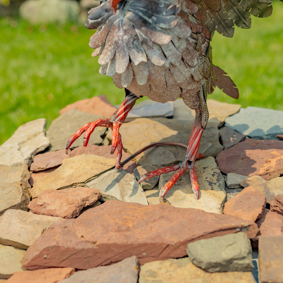 Close view of a metal owl's layered body feathers and red feet standing on flat stones.