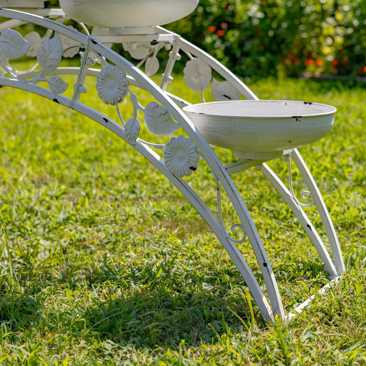 Close side view of the stand’s curved metal legs, floral scrollwork, and two shallow bowls.